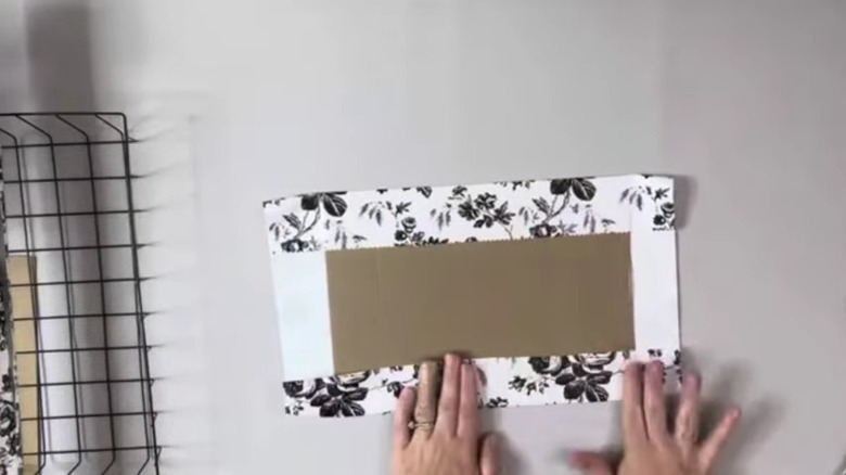 A woman makes a wire shelf liner from a piece of cardboard and self-adhesive wallpaper.