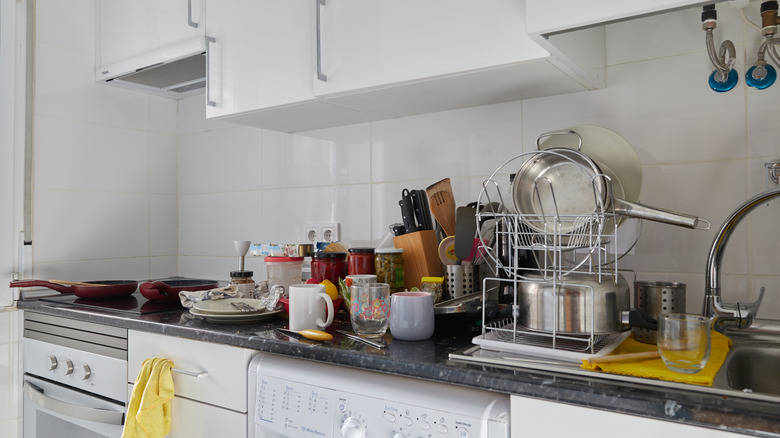 Kitchen with utensils, cups, pans, and kitchenware scattered on the countertop