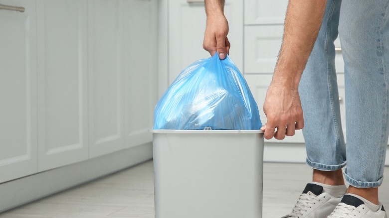 Person pulling blue trashbag out of can