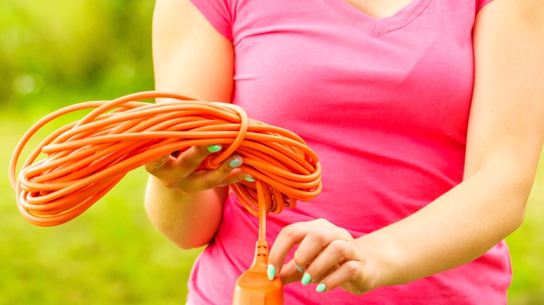 woman in pink shirt holding wrapped up orange extension cord outside