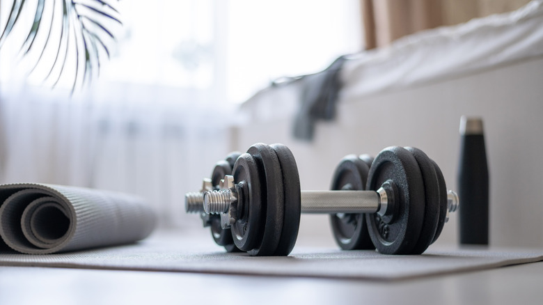 Dumbbells, yoga mat and water bottle on the floor of a room