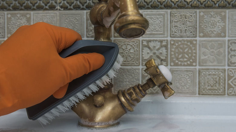 gloved hand brushing bronze faucet