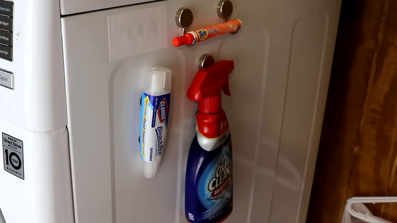 Magnetic buttons and hooks secure laundry essentials to the side of a washing machine.