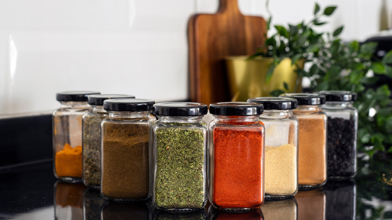 Spices in clear glass bottles lined up on a black kitchen countertop