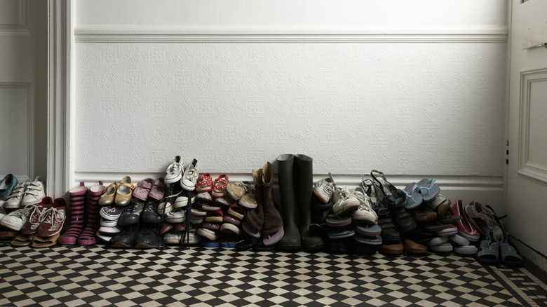 Piles of different types of shoes lined up by the doorway