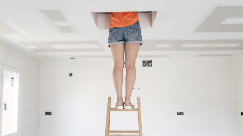 Person on a ladder with their upper body through the attic door opening