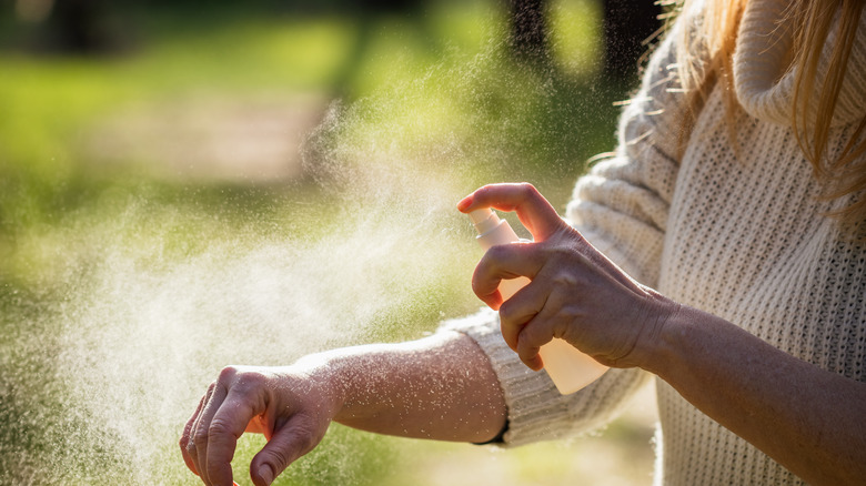 Woman spraying insect repellent on arm