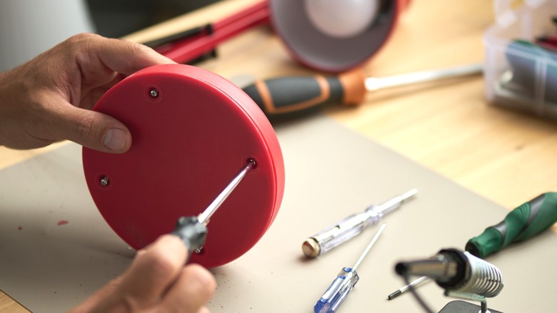 Person installing small screws in bottom of red table lamp