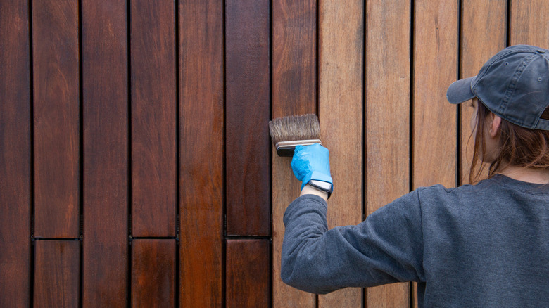 A woman paints a wooden garden fence a darker color