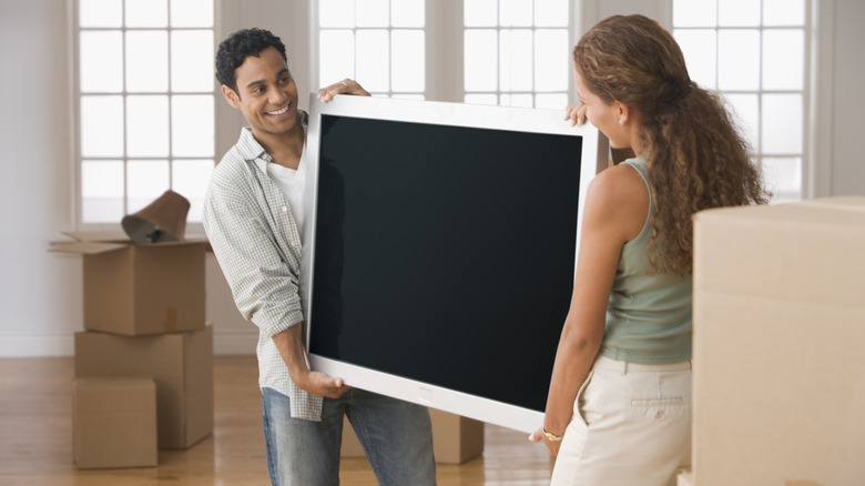 Man and woman moving television near boxes