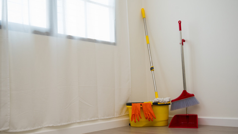 Cleaning supplies, including a broom and mop, tucked in the corner of a room.