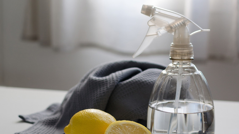 Fresh lemons sit beside a cleaning bottle and towel.