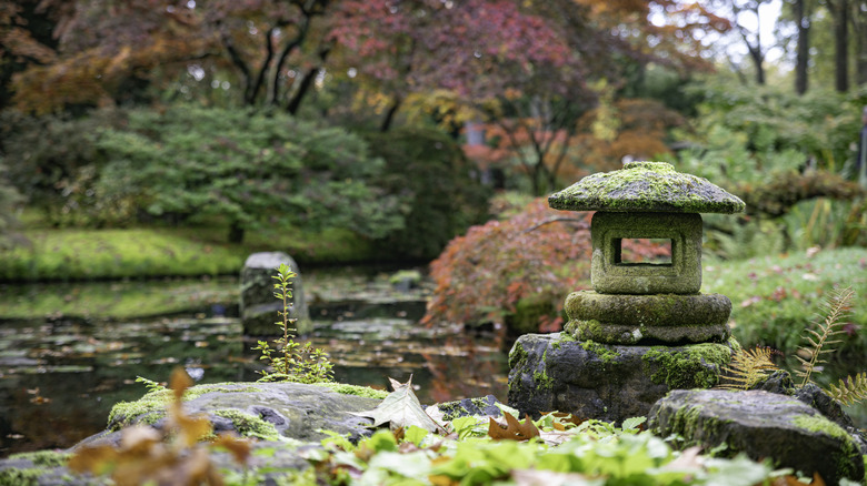 A stone lantern sits on a rock near water in a Japanese garden