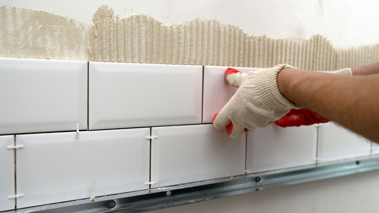 A person installing a white ceramic tile backsplash