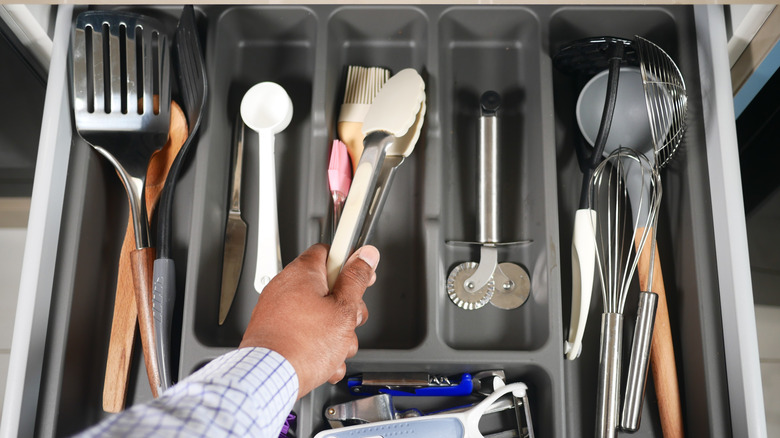 person grabbing thongs from a clean kitchen utensil drawer