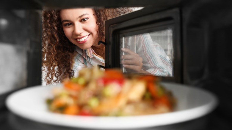 Woman heating food in microwave oven, view from inside