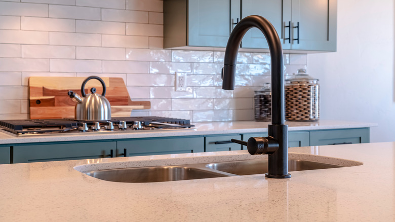 Black faucet and double bowl kitchen island sink against cooktop and cabinets