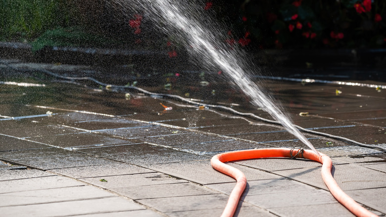 An orange garden hose spouting water through a hole in its side.