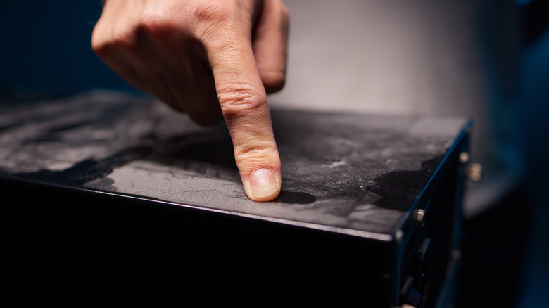 Person's finger smudging white dust on black furniture surface