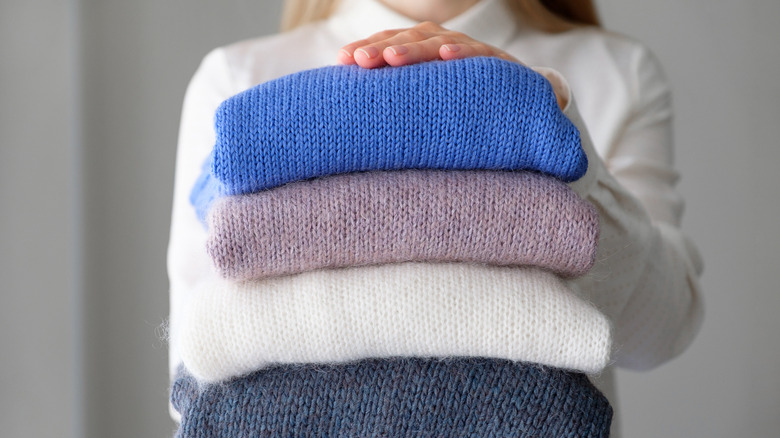 Woman holding stack of three sweaters