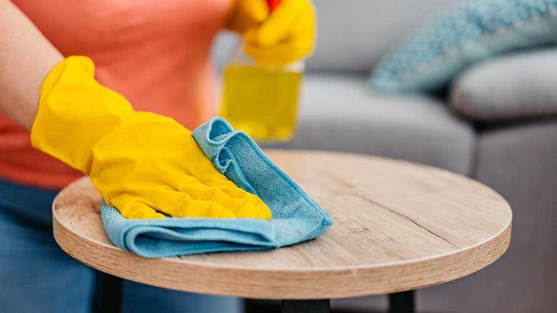 person wiping wood end table