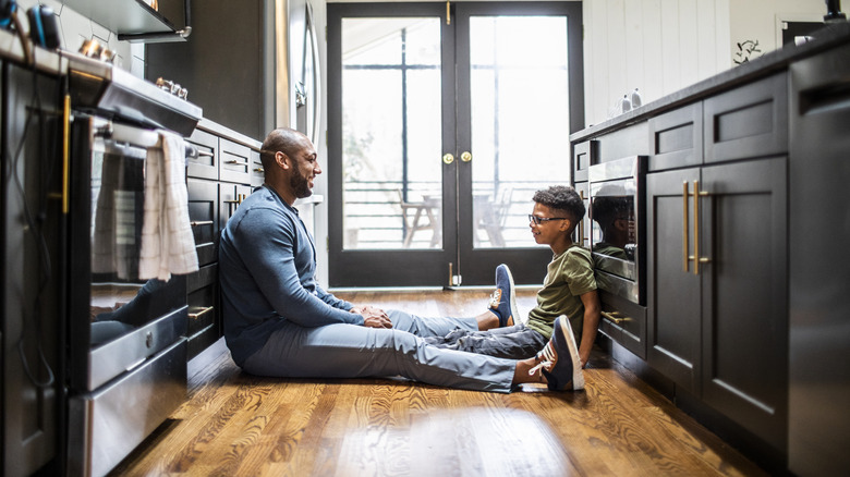 Father and son sitting on hardwood kitchen floor talking