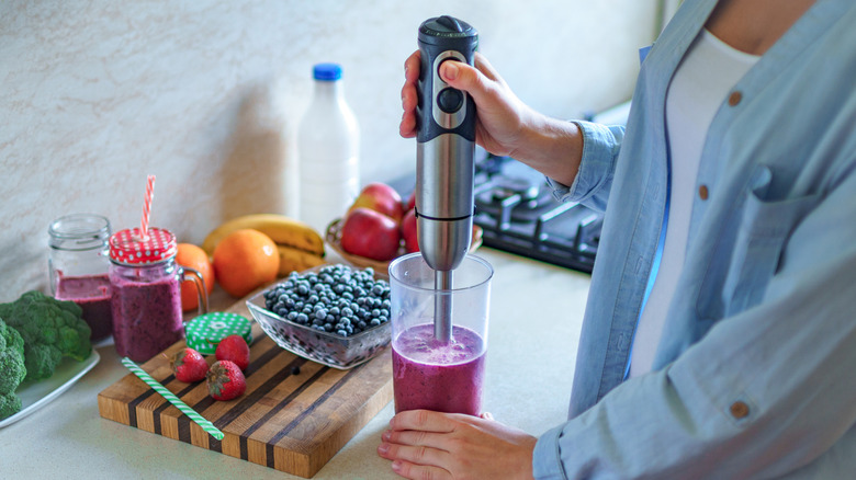 Woman making smoothie with immersion blender