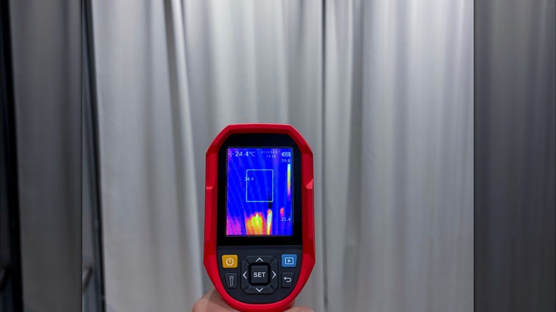 Person using thermal imaging camera to detect where heat loss is occurring through curtain-covered window