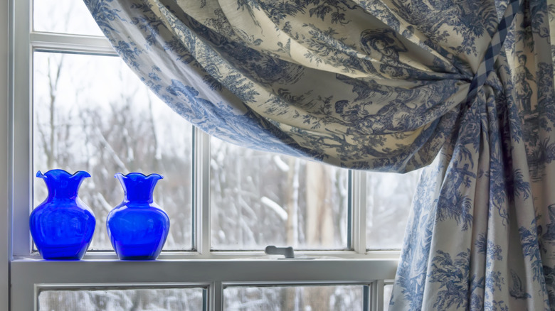 Two bottles standing in the window of a curtained window on a wintery day