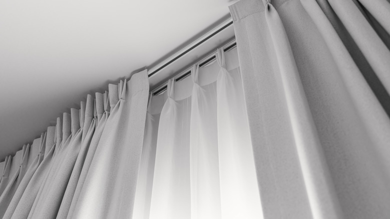 A gray curtain is layered over a white sheer curtain