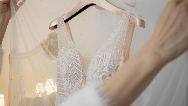 Hands holding up lace behind wedding dress on hanger