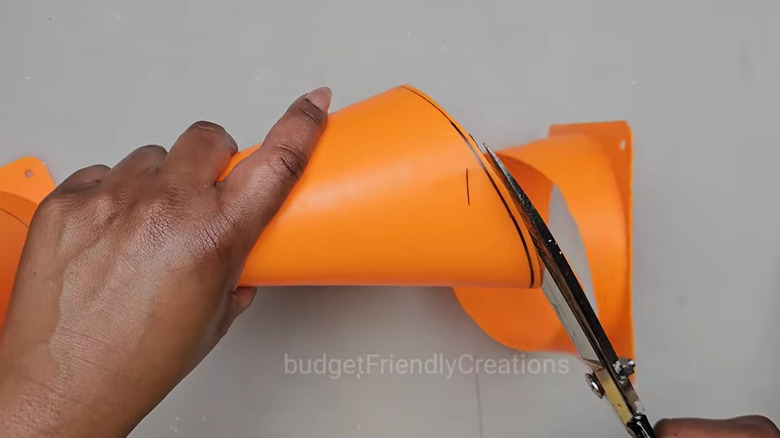 screenshot of YouTube video, black woman's hands cutting orange plastic cone with scissors