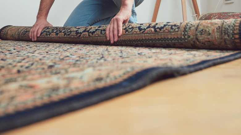 Man rolling out colorful rug in home