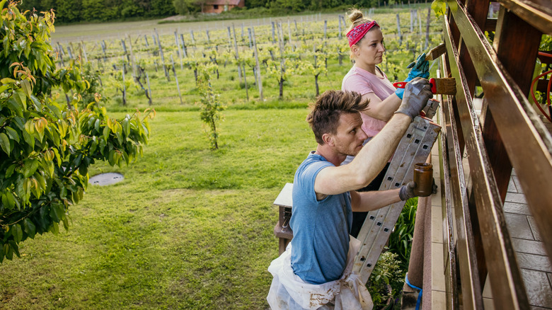 A couple staining a fence railing