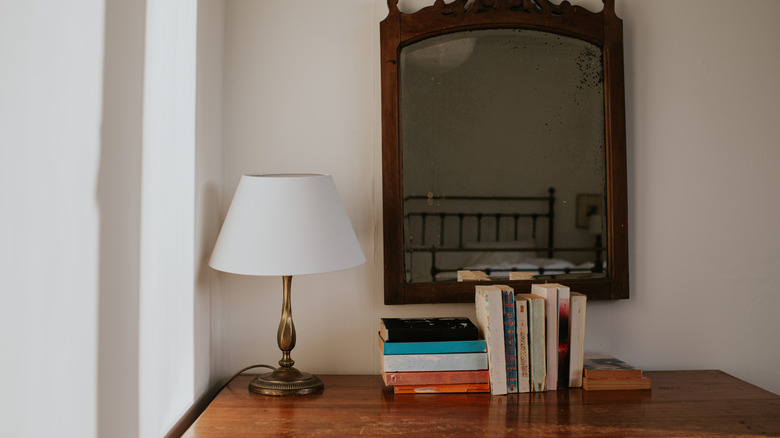 Lamp sitting on a table with books and a mirror