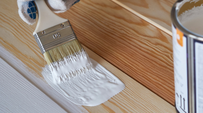 Paintbrush transferring white paint onto wood