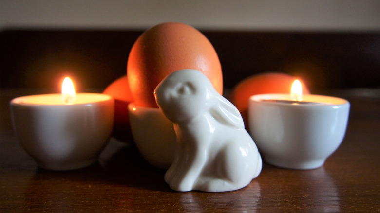 Lighted candles, a bunny figurine, and eggs displayed on a table