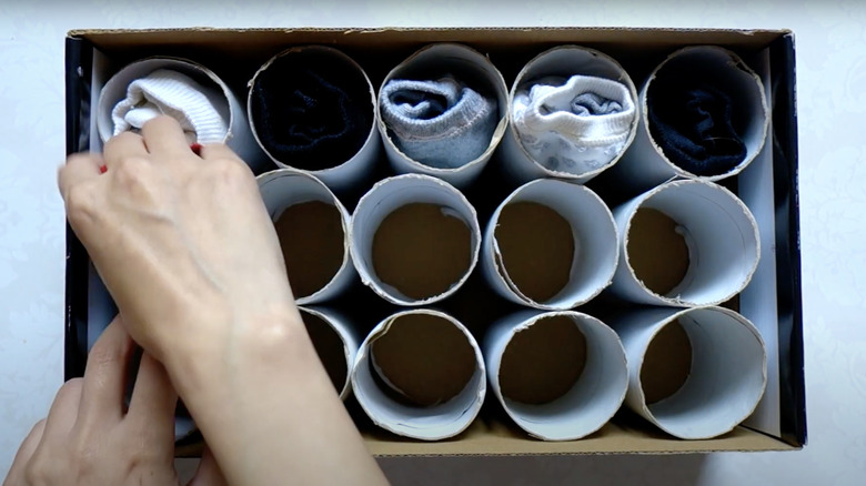 woman tucking sock pairs into toilet paper roll box