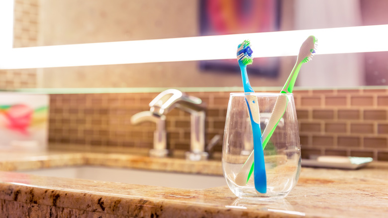 Two toothbrushes sitting in a drinking glass on a counter.