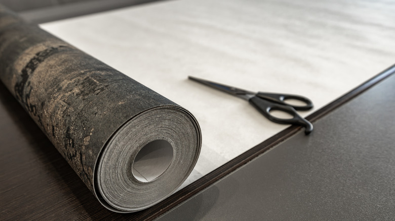 A roll of wallpaper and a pair of scissors sit on a countertop.