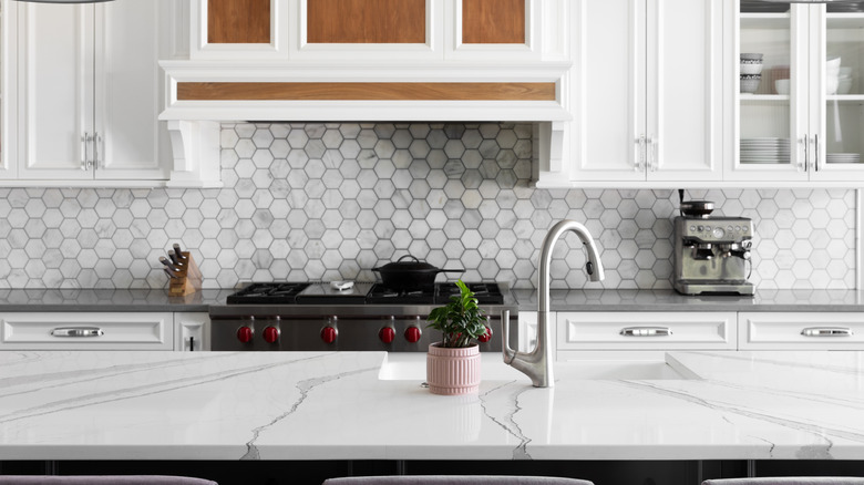 A white kitchen with hexagonal backsplash and large white marble kitchen island.