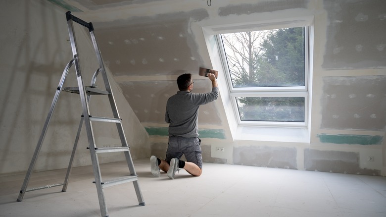 Man sanding attic wall