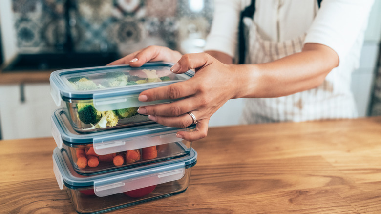 Female hands stacking glass storage containers with vegetables on counter