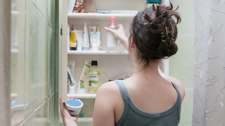 Woman grabbing two products out of bathroom medicine cabinet