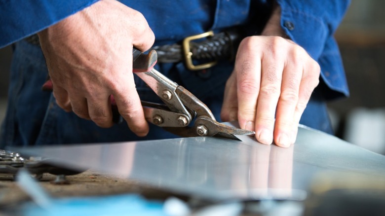 Man cutting piece of metal sheet with rusty tin snips