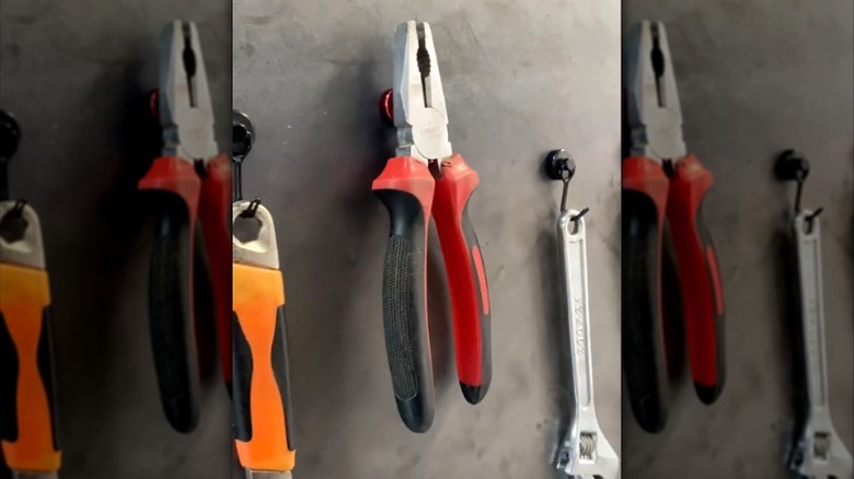 Pliers and two wrenches hanging on magnetic hooks on metal sheet