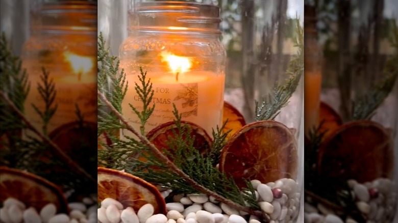 Candle surrounded by white beans, pine, and decorative dried orange slices