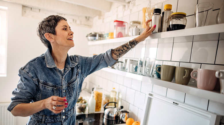 Person placing a metal water bottle on top of a kitchen shelf