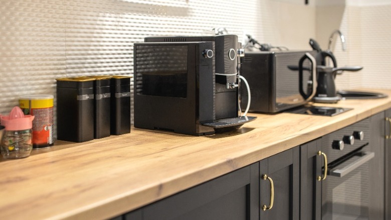 Black coffee maker, microwave, and spice jars on wood counter over black cabinets