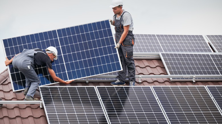 Builders carry solar panels on an asphalt roof